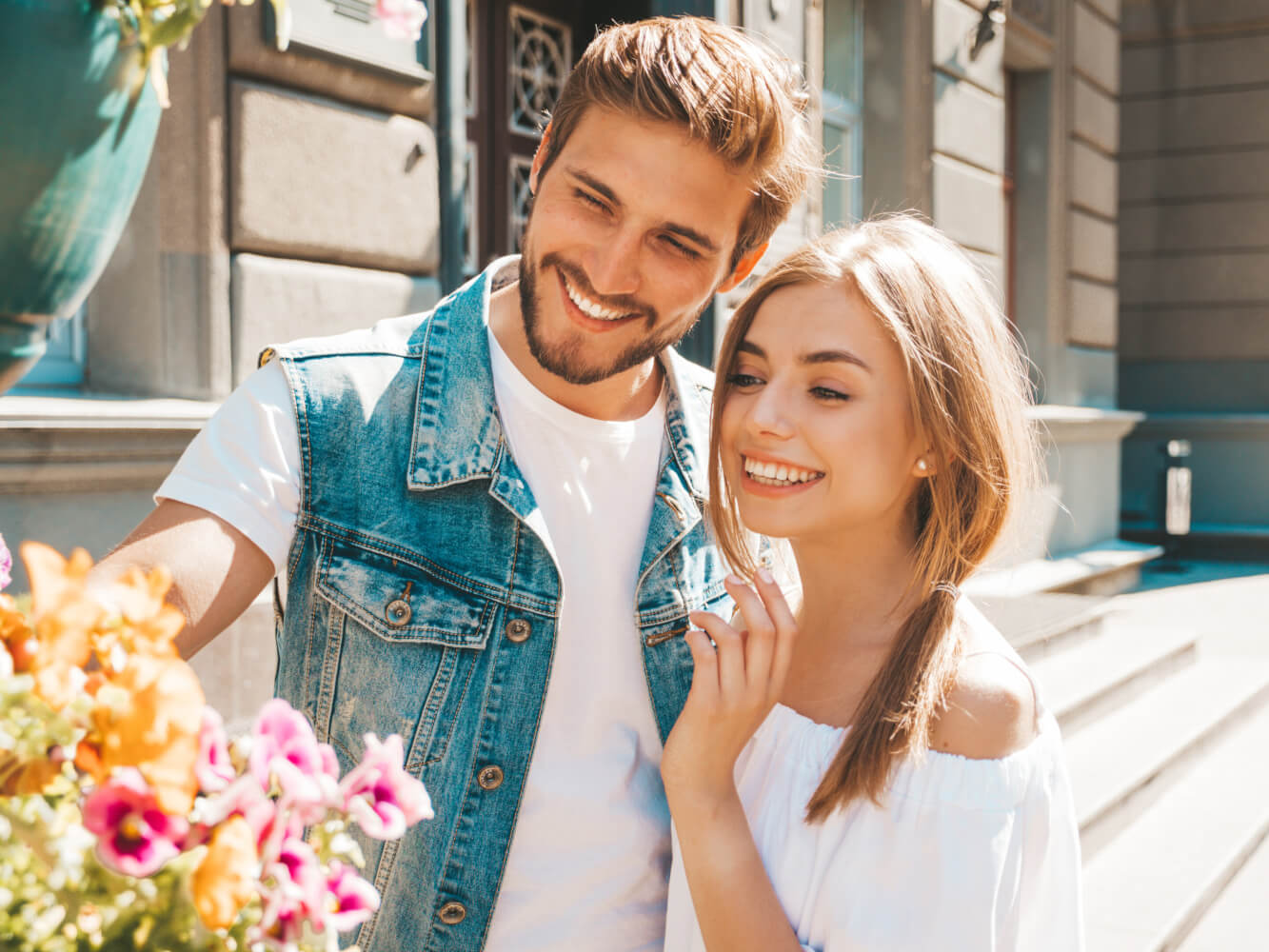 Smiling beautiful girl and her handsome boyfriend. Woman in casual summer dress and man in jeans clothes. Happy cheerful family. Female having fun on the street background.Looking at flowers